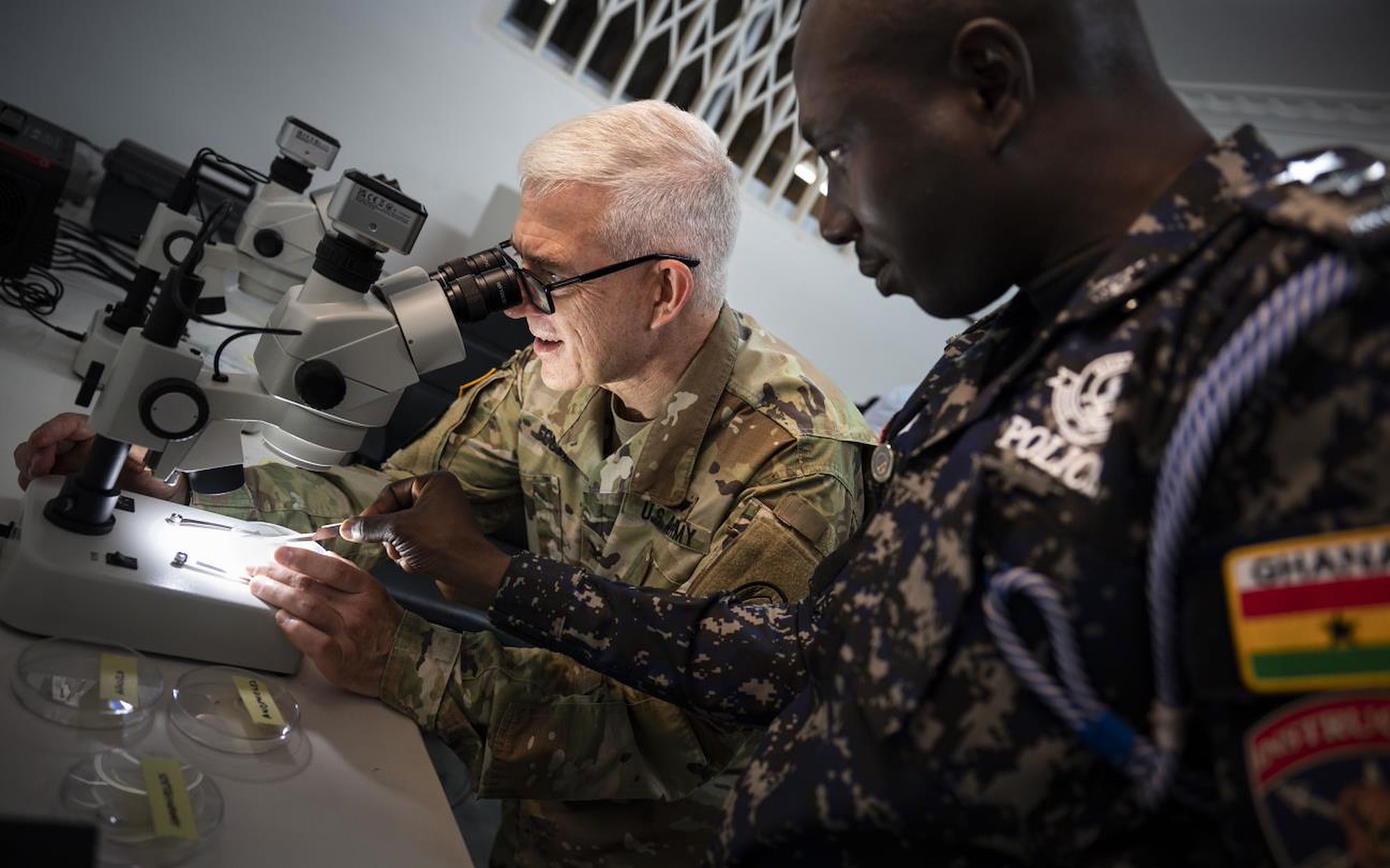 U.S. Army Col. Tom Eccles, United States Africa Command surgeon, identifies different mosquito species through a microscope with Deputy Superintendent of Police Emmanuel Baba Asabila, Ghana Police.